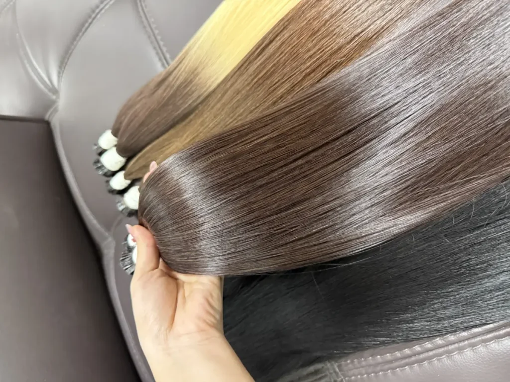 Bàn tay cầm nhiều bó tóc nối màu nâu và khói, thấy rõ mối keratin trắng ở đầu tép và độ bóng của thân tóc