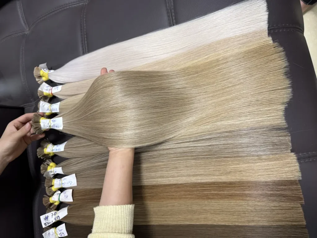 Các bó tóc nối xếp cạnh nhau theo thang màu từ bạch kim tới nâu, mỗi bó buộc nhãn viết tay ghi mã màu, độ dài và khối lượng